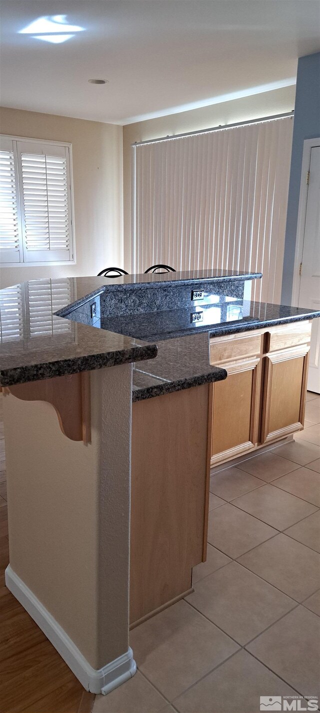 kitchen featuring a kitchen bar, a kitchen island, dark stone countertops, and light tile patterned floors