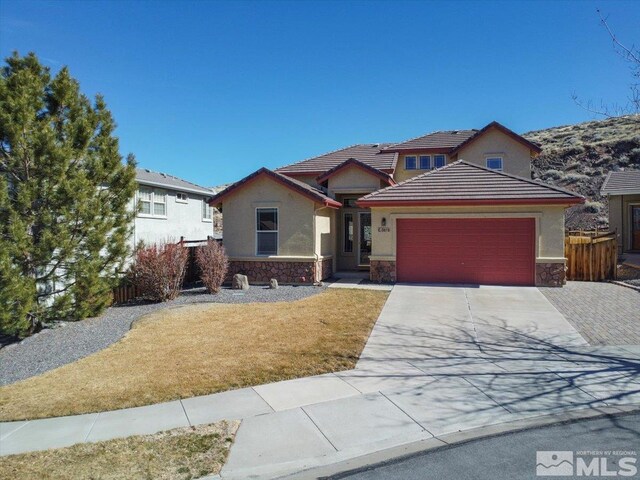 view of front facade with an attached garage, fence, stone siding, driveway, and stucco siding