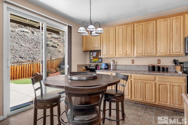 kitchen with tile countertops, light brown cabinets, stainless steel microwave, and hanging light fixtures