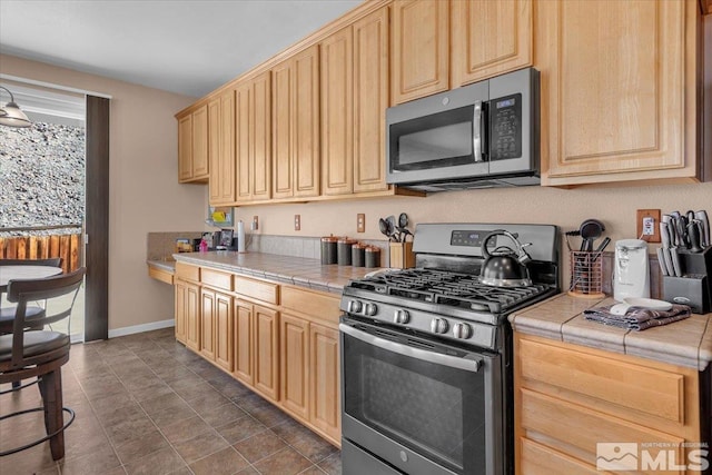 kitchen featuring stainless steel appliances, tile counters, baseboards, and light brown cabinetry