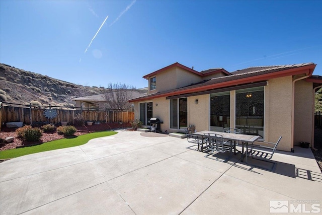 rear view of property featuring outdoor dining area, a patio area, fence, and stucco siding