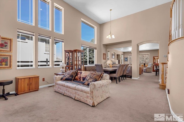 carpeted living area featuring a chandelier, arched walkways, and baseboards