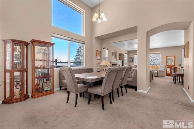 dining room with baseboards, arched walkways, a towering ceiling, carpet flooring, and a notable chandelier