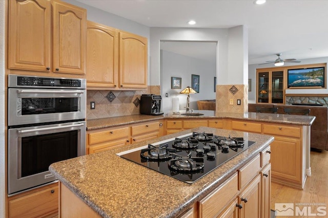 kitchen with a kitchen island, black gas cooktop, light brown cabinetry, light wood-type flooring, and double oven