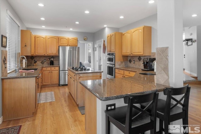 kitchen with dark stone counters, appliances with stainless steel finishes, light wood-type flooring, and a sink