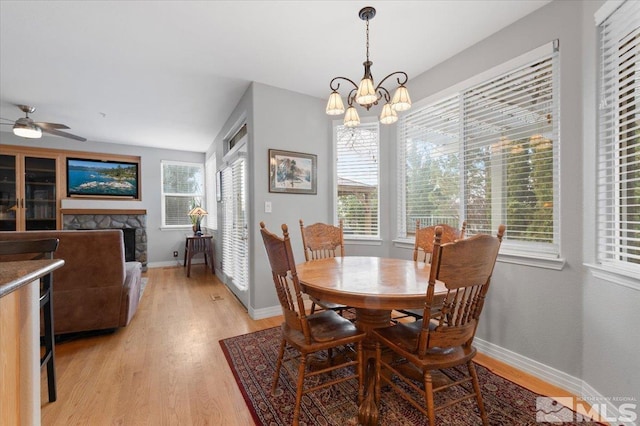 dining room featuring baseboards, plenty of natural light, a stone fireplace, and light wood finished floors