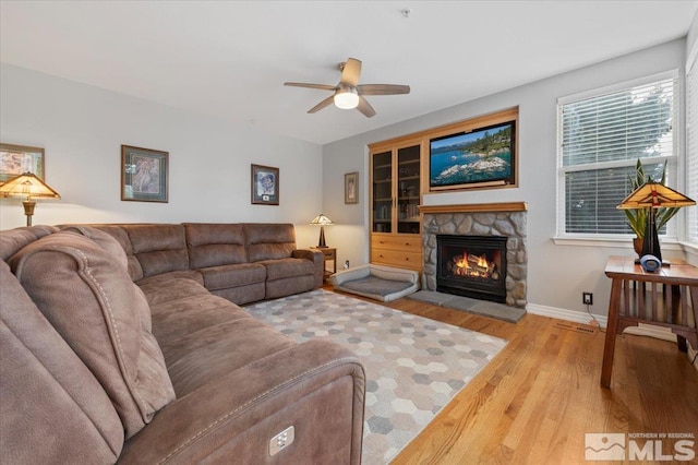 living area featuring ceiling fan, a fireplace, wood finished floors, visible vents, and baseboards