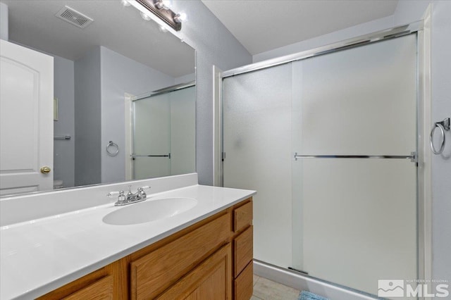 bathroom featuring vanity, a shower stall, and visible vents