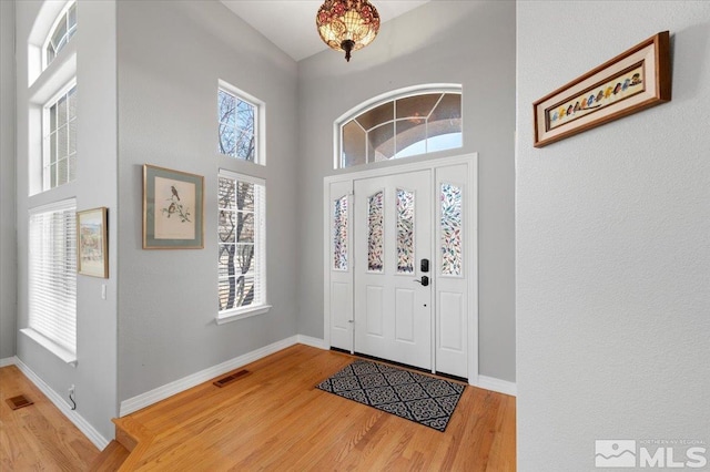 entrance foyer featuring a towering ceiling, wood finished floors, visible vents, and baseboards