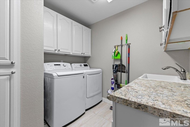 clothes washing area featuring light tile patterned floors, cabinet space, a sink, independent washer and dryer, and baseboards