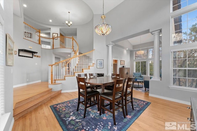 dining area with decorative columns, a towering ceiling, and wood finished floors