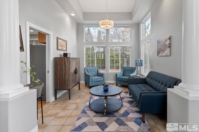 sitting room with light tile patterned floors, a raised ceiling, ornate columns, a high ceiling, and baseboards