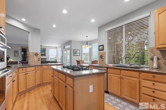 kitchen featuring stainless steel appliances, dark stone countertops, a sink, and light wood-style flooring