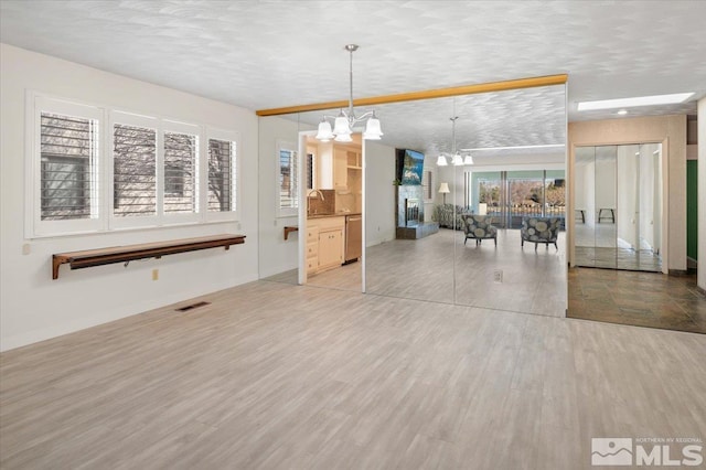 dining room featuring baseboards, visible vents, a textured ceiling, light wood-style floors, and a notable chandelier