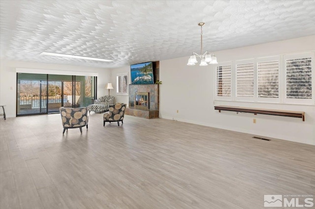 sitting room with visible vents, wood finished floors, a textured ceiling, a fireplace, and a chandelier