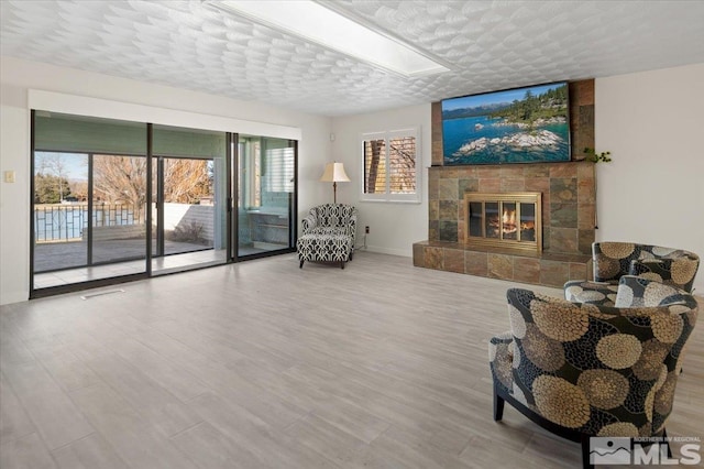 sitting room with a tile fireplace, a textured ceiling, baseboards, and wood finished floors