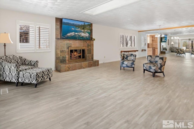 living room with a textured ceiling, a tile fireplace, wood finished floors, and a notable chandelier