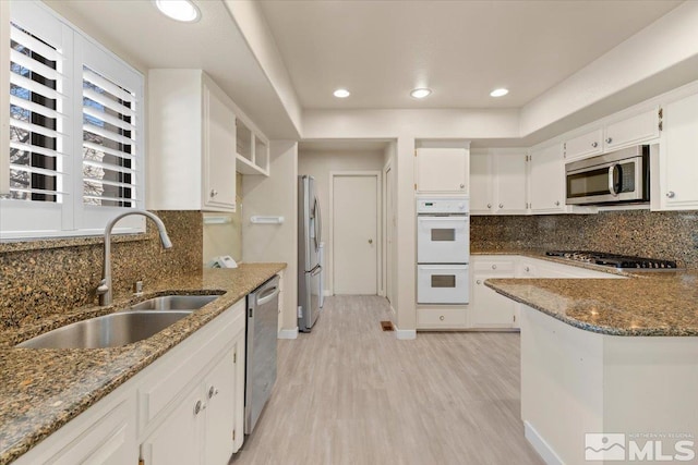 kitchen with light wood finished floors, appliances with stainless steel finishes, dark stone countertops, white cabinetry, and a sink