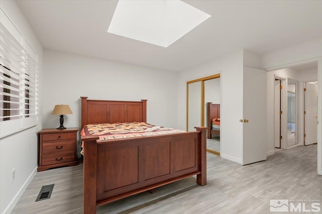 bedroom with light wood-style flooring, a skylight, visible vents, baseboards, and a closet