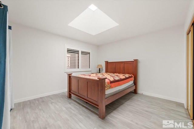 bedroom with light wood-style floors, a skylight, and baseboards