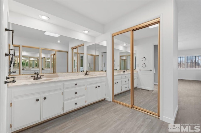 bathroom with double vanity, baseboards, wood finished floors, a sink, and recessed lighting