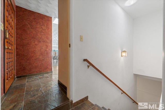 hallway with an upstairs landing, baseboards, visible vents, and stone tile floors