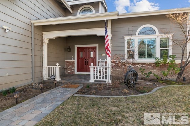 doorway to property featuring a porch and brick siding