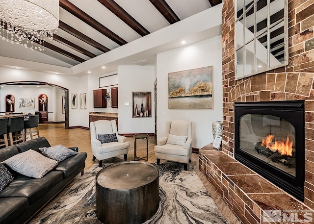 living area featuring arched walkways, vaulted ceiling with beams, recessed lighting, a large fireplace, and baseboards