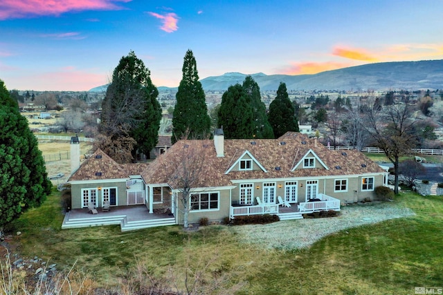 back of house at dusk featuring french doors, a yard, and a deck with mountain view