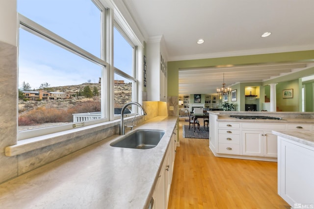 kitchen featuring a sink, gas stovetop, white cabinets, light wood-type flooring, and crown molding