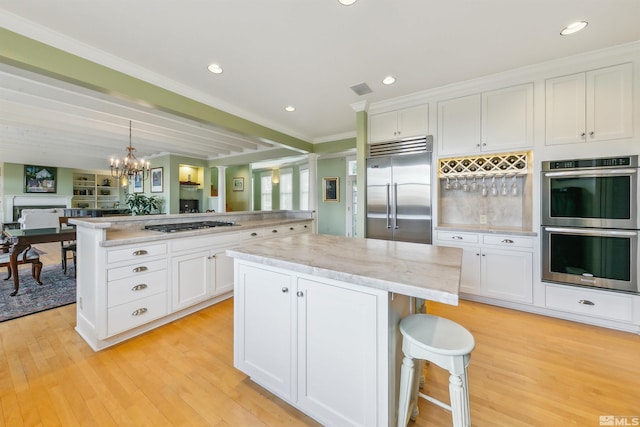 kitchen featuring stainless steel appliances, white cabinetry, open floor plan, light wood-type flooring, and a center island