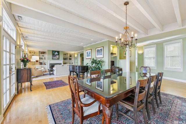 dining room with light wood-style flooring, beam ceiling, a chandelier, and a lit fireplace