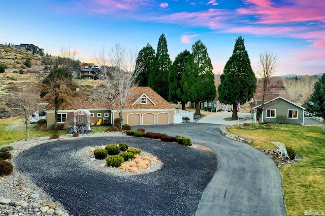 view of front facade with curved driveway, an attached garage, and a lawn