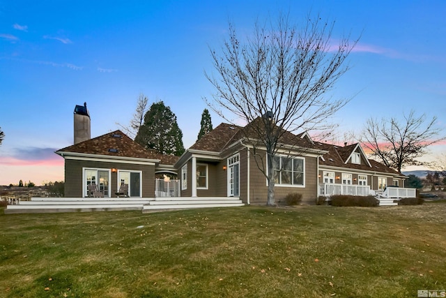 back of house at dusk featuring a lawn and a chimney