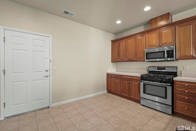 kitchen with light countertops, visible vents, appliances with stainless steel finishes, brown cabinetry, and baseboards