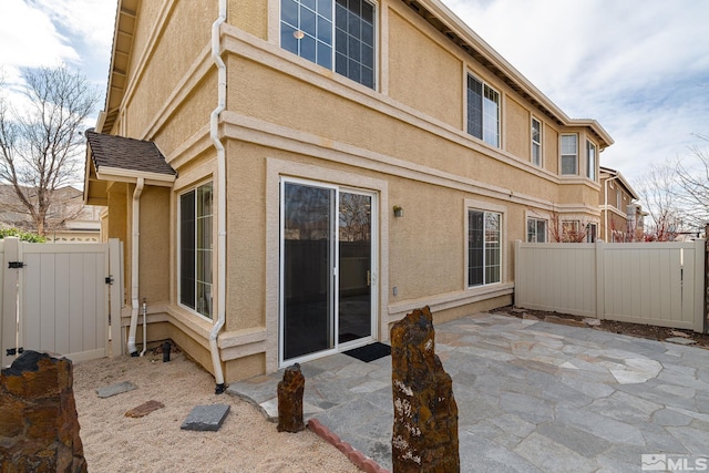 rear view of house featuring a patio area, fence, a gate, and stucco siding