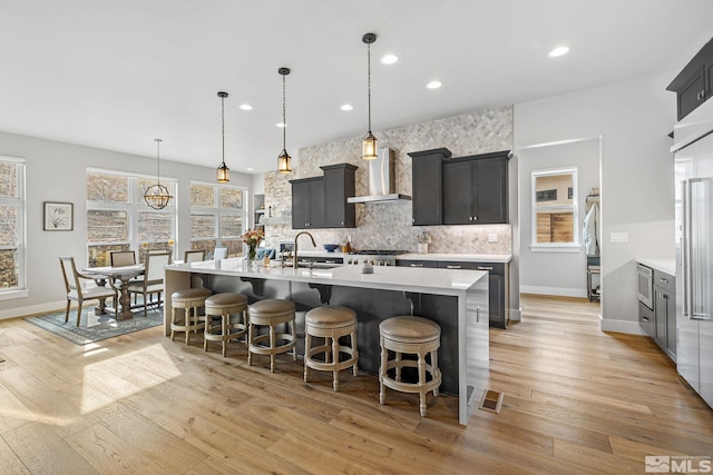 kitchen featuring tasteful backsplash, light wood-type flooring, light countertops, and wall chimney range hood