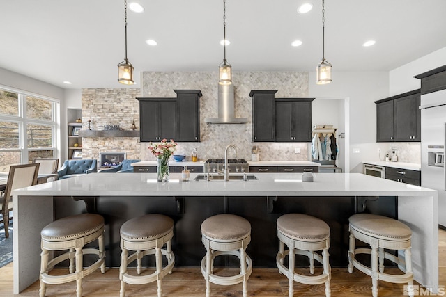 kitchen with light countertops, light wood-style flooring, backsplash, a sink, and wall chimney exhaust hood