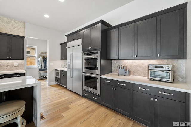 kitchen with stainless steel appliances, dark cabinets, light countertops, and light wood-style floors