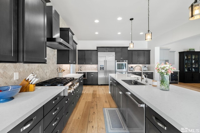 kitchen with wall chimney exhaust hood, appliances with stainless steel finishes, a sink, and dark cabinets