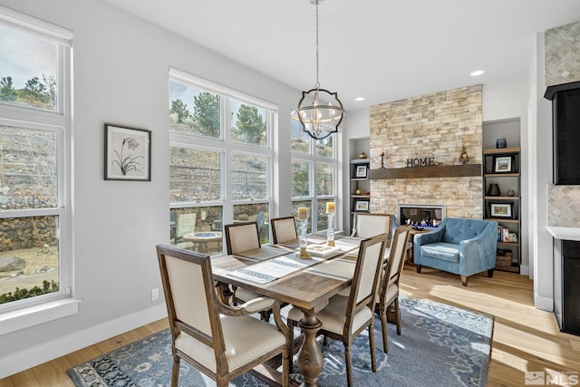 dining space with a stone fireplace, recessed lighting, baseboards, light wood-type flooring, and an inviting chandelier