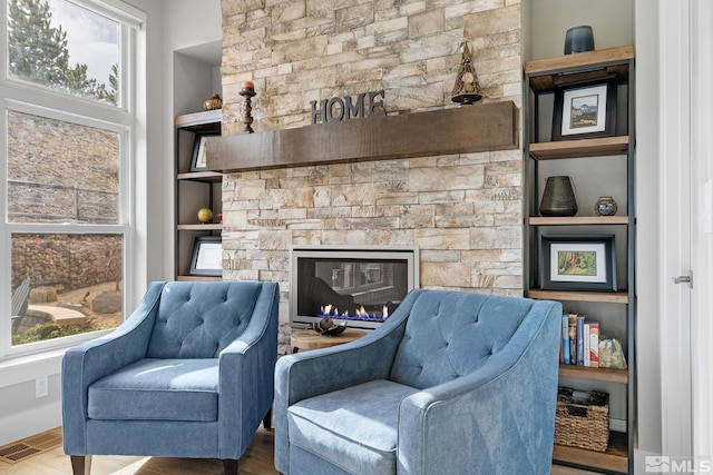 sitting room with built in shelves, a fireplace, visible vents, and wood finished floors