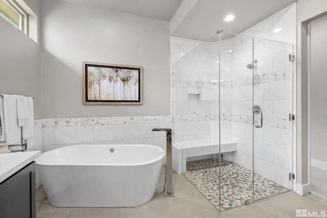 bathroom with a stall shower, tile patterned floors, vanity, a freestanding tub, and tile walls