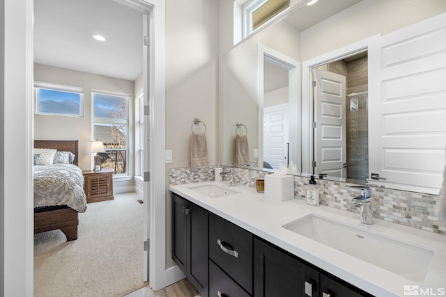 ensuite bathroom with double vanity, connected bathroom, backsplash, and a sink