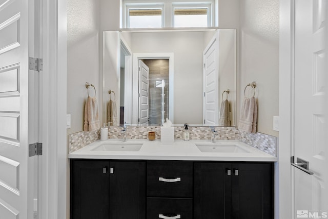 full bath featuring an enclosed shower, double vanity, tasteful backsplash, and a sink