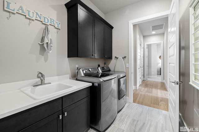 laundry room with washing machine and clothes dryer, cabinet space, visible vents, light wood-style floors, and a sink