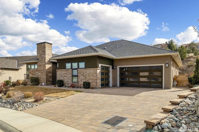 view of front of house featuring a garage, a shingled roof, stone siding, decorative driveway, and stucco siding