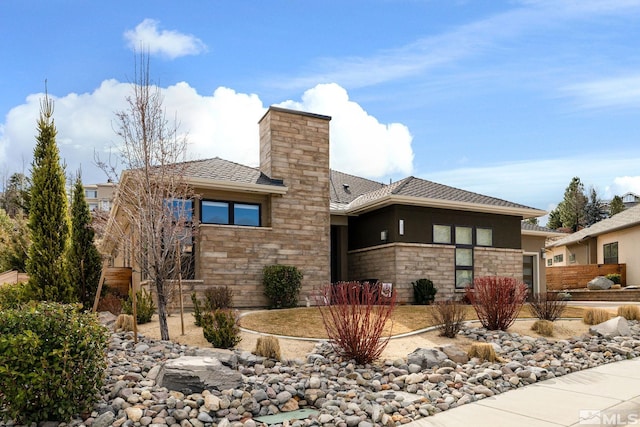 prairie-style home with stone siding, a chimney, an attached garage, and stucco siding