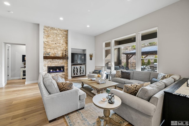 living room featuring light wood-type flooring, recessed lighting, baseboards, and a stone fireplace