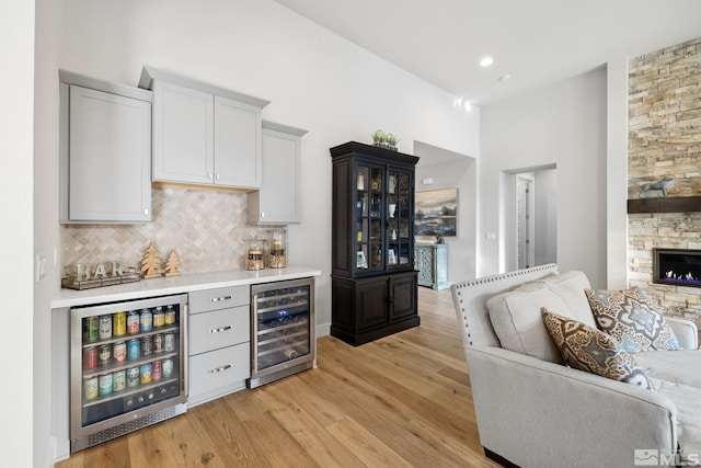 bar with tasteful backsplash, wine cooler, light wood-style flooring, and a bar